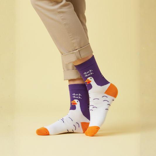 Mor manşetli, beyaz zemin üzerinde ördek illüstrasyonlu ve turuncu burun-topuk detaylı duck. duck. yazılı soket çorap.