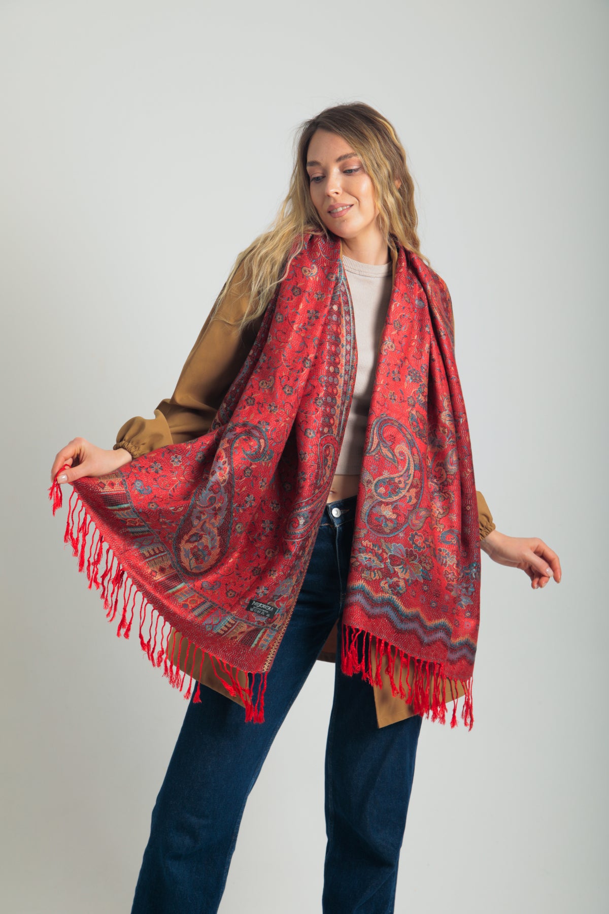Kırmızı paisley desenli pashmina şal – kadın modeli tarafından tutulmuş, püsküllü kenarlı, geleneksel motifli şık şal