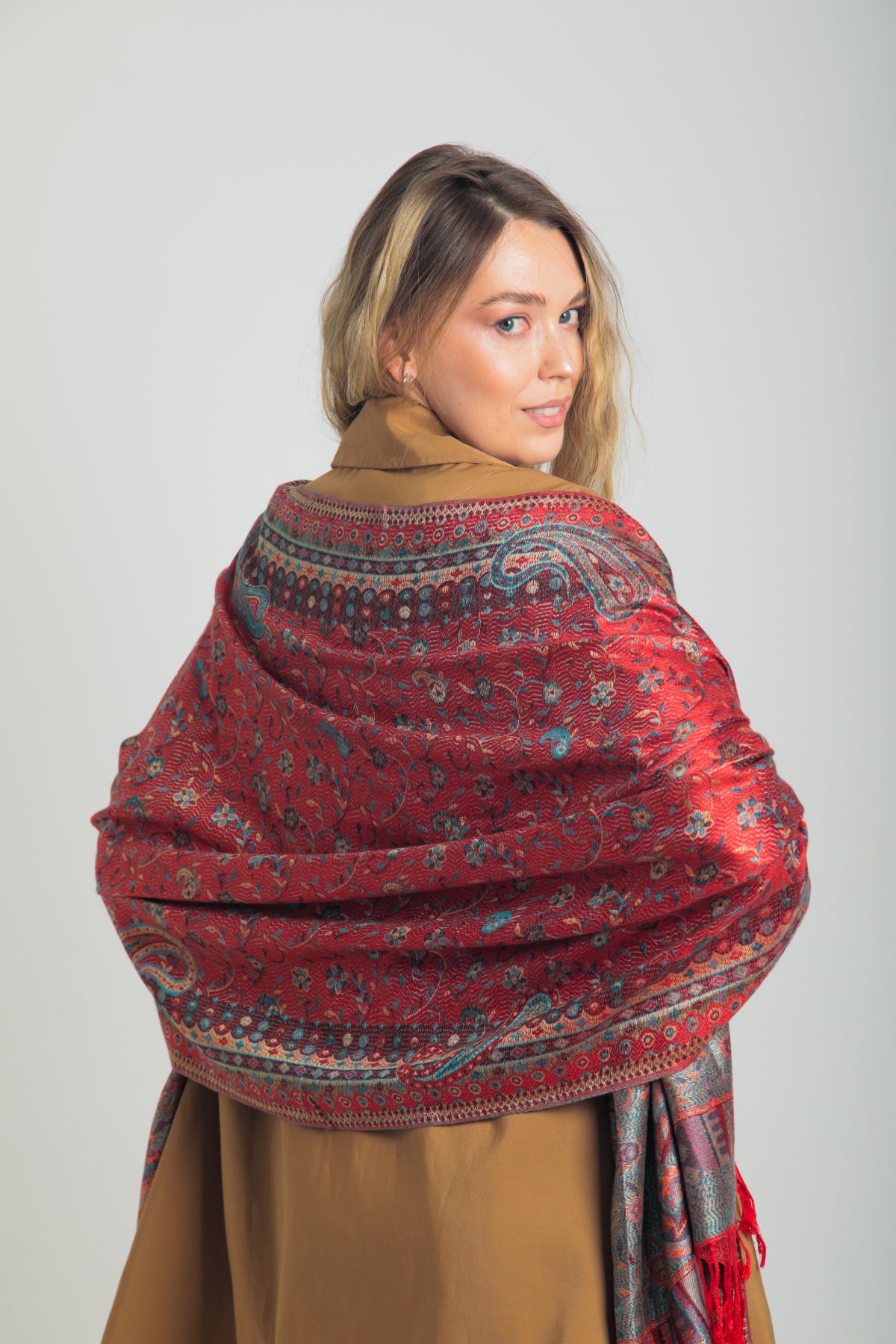 Kırmızı paisley desenli pashmina şal – kadın modeli tarafından tutulmuş, püsküllü kenarlı, geleneksel motifli şık şal