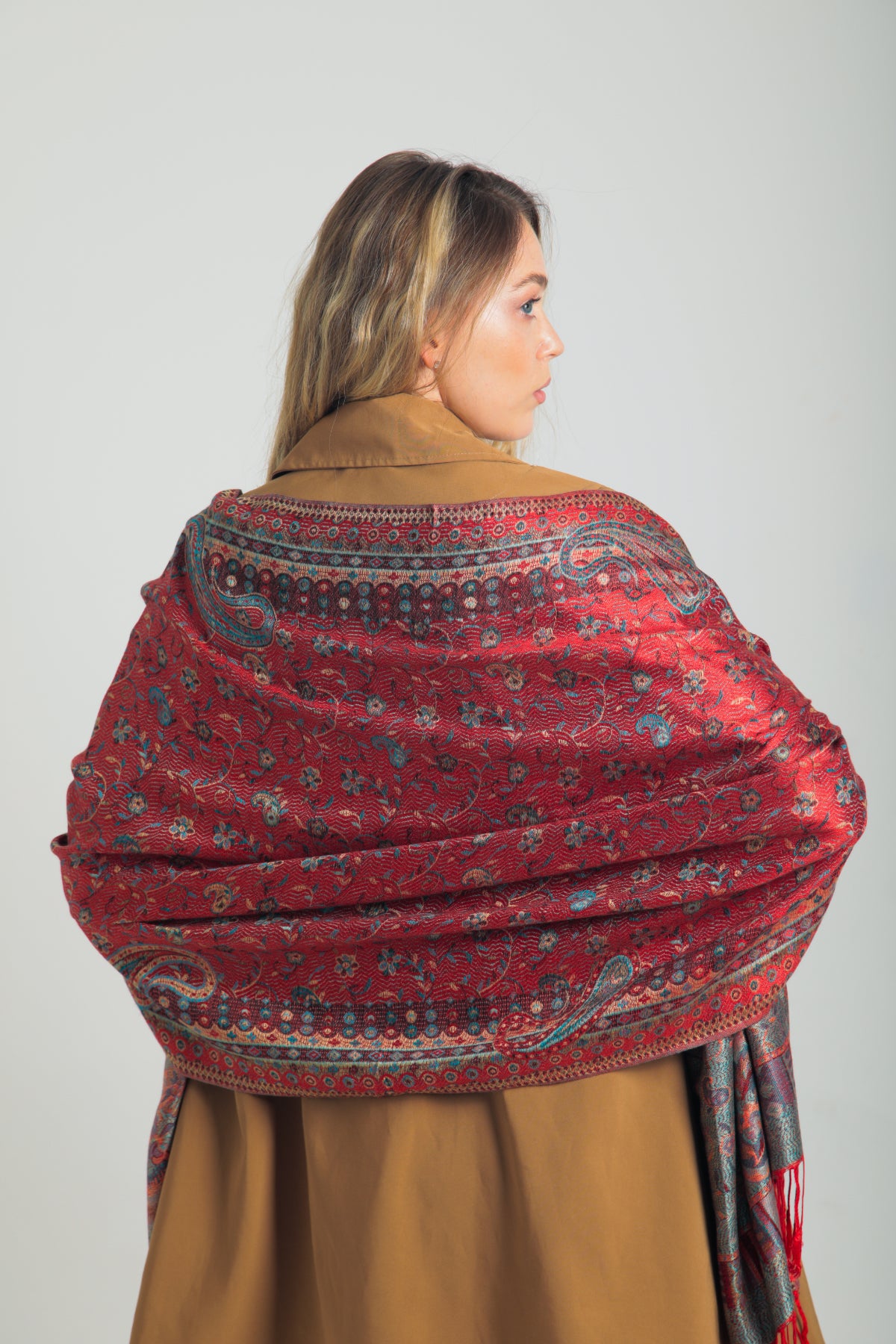 Kırmızı paisley desenli pashmina şal – kadın modeli tarafından tutulmuş, püsküllü kenarlı, geleneksel motifli şık şal